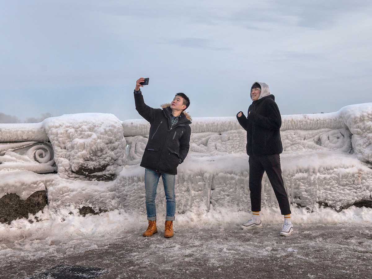 Visitors take a selfie as ice and snow coat a railing