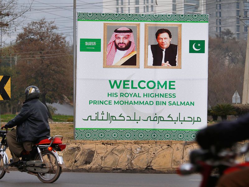 Pakistani motorcyclists pass by a billboard
