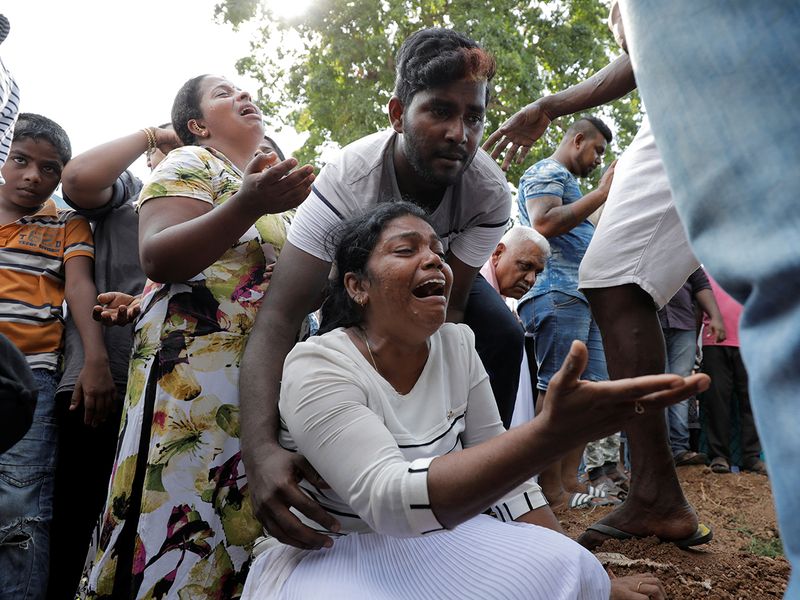 People react during a mass burial of victims