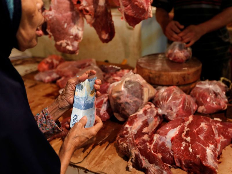 A woman holds rupiah bank notes as she shops for meat