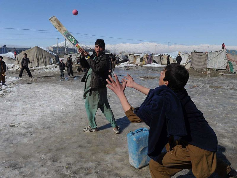 Internally displaced Afghan children play cricket in a refugee camp