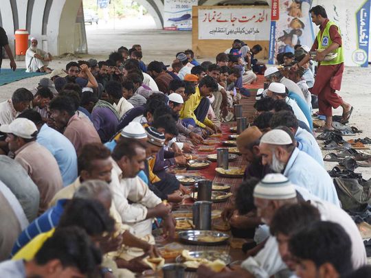 People eat charity food by a roadside in Karachi