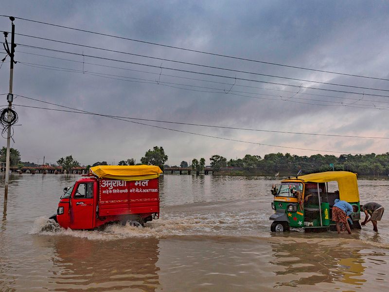 Boys stand by an autorickshaw in a flooded street in Prayagraj, in the northern Indian state of Uttar Pradesh