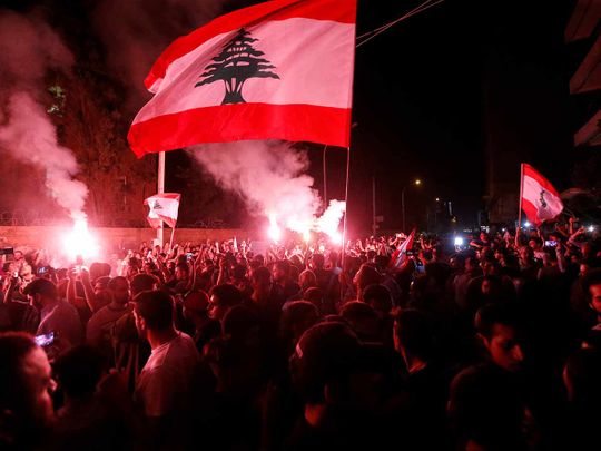 Demonstrators hold flares and Lebanese flags as they protest outside the house of former Lebanese prime minister Fouad Siniora in Beirut