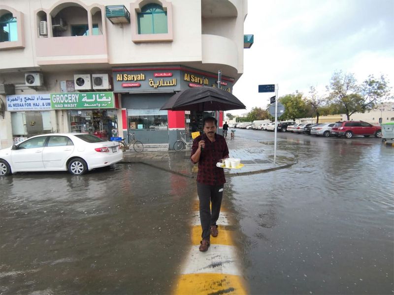 A man crosses a flooded street in Sharjah with an umbrella while raining in Sharjah. 
