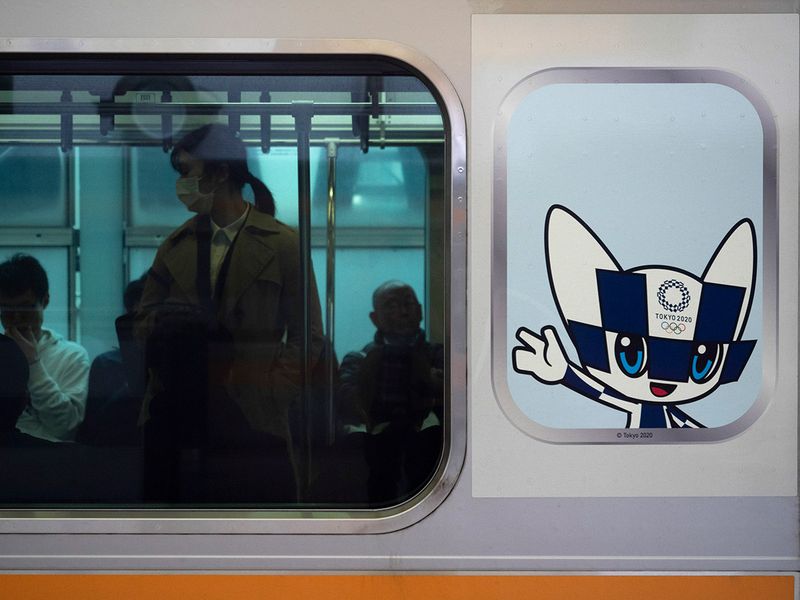 Commuters sit in a train carrying a poster showing the Tokyo 2020 Olympics mascot, Miraitowa, in Tokyo