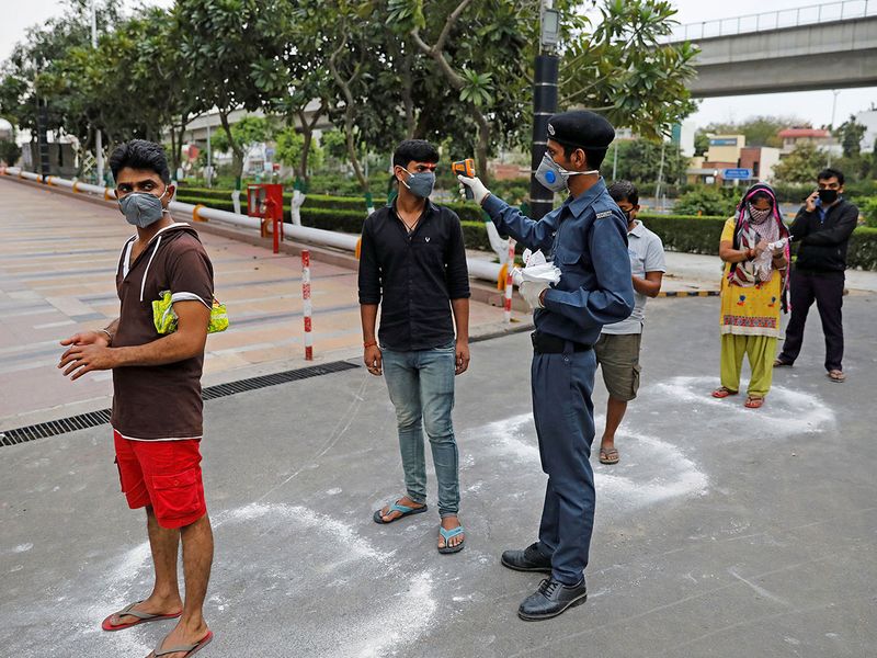 A private security guard uses an infrared thermometer to measure the temperature of people standing in circles drawn with chalk to maintain safe distance as they wait to enter a supermarket during the coronavirus disease outbreak in New Delhi.