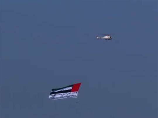UAE flag with the message #DedicationatWorkandSafetyatHome flown over Abu Dhabi