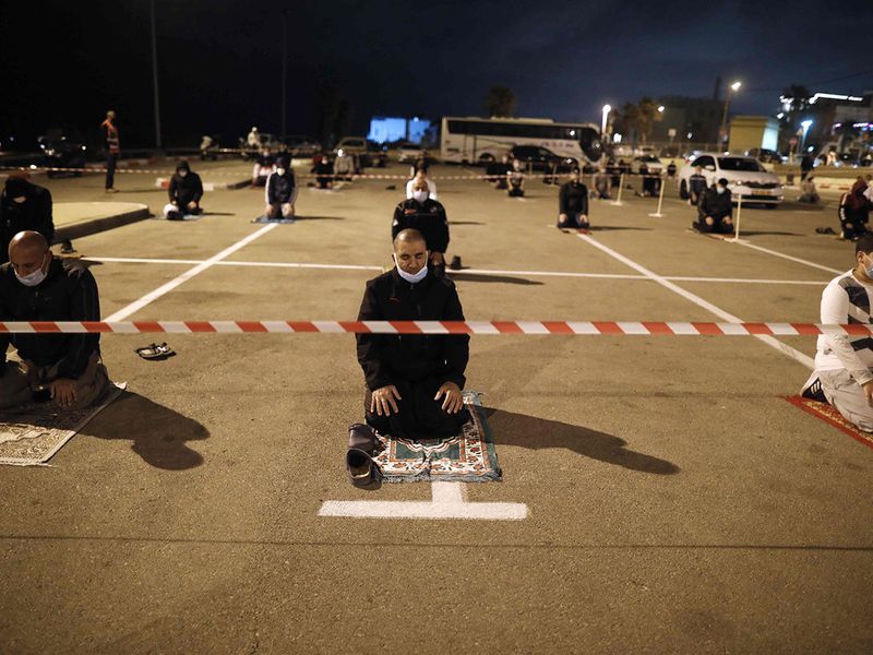 Palestinian and Arab Israeli men keep a 2-meter distance amid the COVID-19 pandemic, as they pray in a parking lot near the beach in Jaffa, near the Israeli coastal city of Tel Aviv after breaking their fast.  Mosques stood empty and fast-breaking feasts were cancelled as Muslims around the world began marking Ramadan under the novel coronavirus lockdown, while a pushback in some countries sparked fears of a surge in infections.