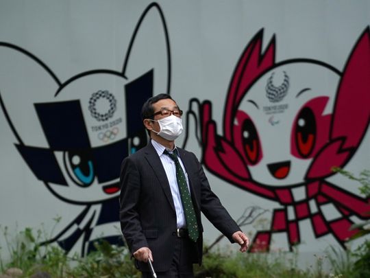 A man with a face mask walks in front of Miraitowa and Someity, mascots for the Tokyo 2020 Olympics and Paralympics at a park in Tokyo.