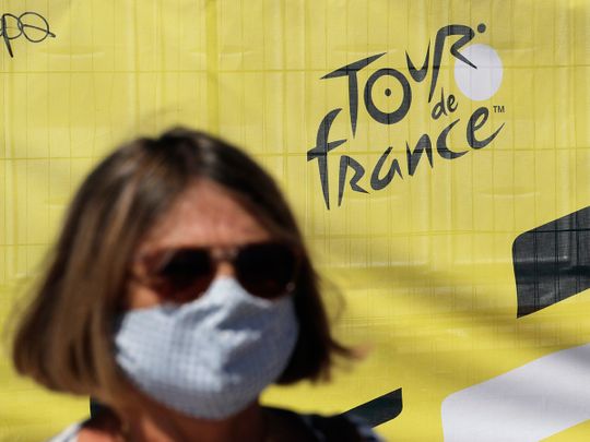 A woman wears a face mask as she walks past a Tour de France logo in Nice