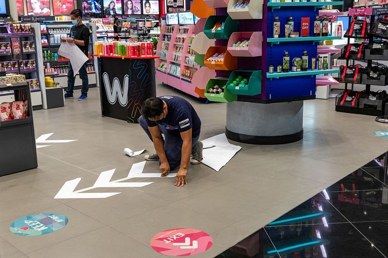 A man wearing a protective mask positions social distancing floor signs at a Watson's store in the Dubai Mall in Dubai.