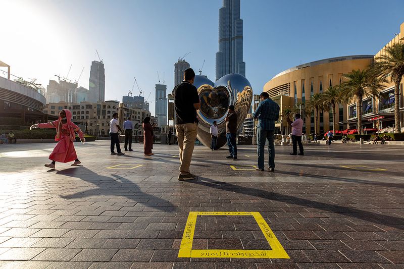 Tourists wearing protective masks stand among social distancing floor signs outside the Dubai Mall near the Burj Khalifa skyscraper in Dubai.
