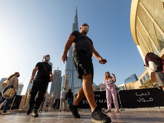 Tourists wearing protective masks walk near the Dubai Mall and the Burj Khalifa skyscraper in Dubai.