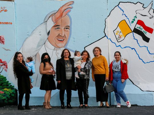 Iraqi Christians pose for photo near a mural of Pope Francis on the wall of a church upon his upcoming visit to Iraq, in Baghdad