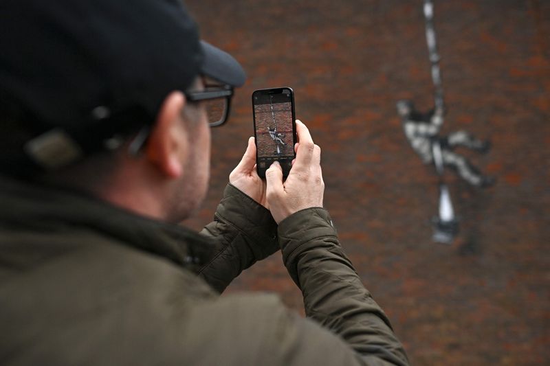 In this file photo taken on March 02, 2021 Members of the public pause to look at an artwork by street artist Banksy on the side of Reading Prison in Reading, west of London.