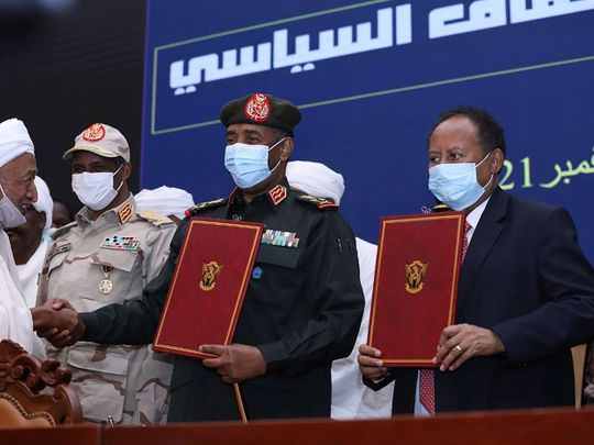 In this photo provided by the Sudan Transitional Sovereign Council, Sudan's top general Abdel Fattah Al Burhan, centre, and Prime Minister Abdalla Hamdok hold documents during a ceremony to reinstate Hamdok, who was deposed last month, in Khartoum on November 21, 2021.