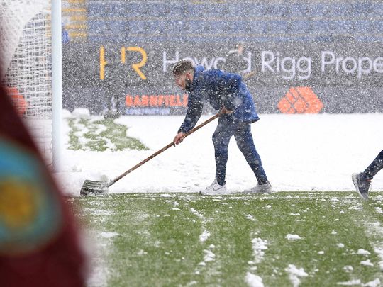 Groundstaff try to clear the pitch in a blizzard before Burnley v Tottenham was called off