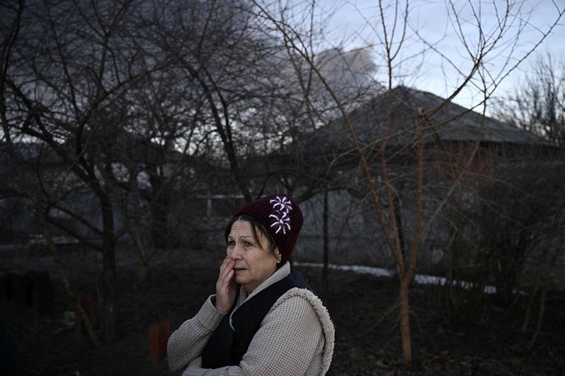 A woman stands in a street as black smoke rises from a military airport in Chuguyev near Kharkiv. 