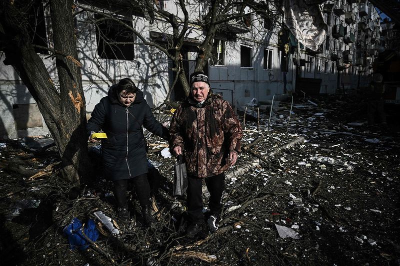 People walk past the body of a relative outside a destroyed building after bombings on the eastern Ukraine town of Chuguiv.