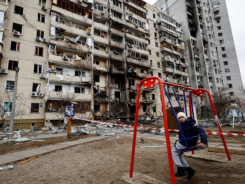 A child sits on a swing in front of a damaged residential building, after Russia launched a massive military operation against Ukraine, in Kyiv, Ukraine.