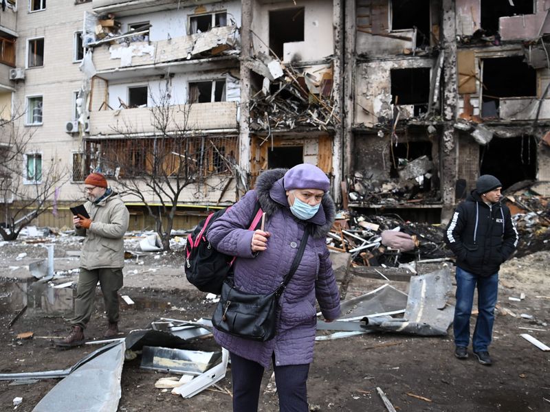 A woman with a backpack walks in front of a damaged residential building at Koshytsa Street, a suburb of the Ukrainian capital Kyiv, where a military shell allegedly hit.