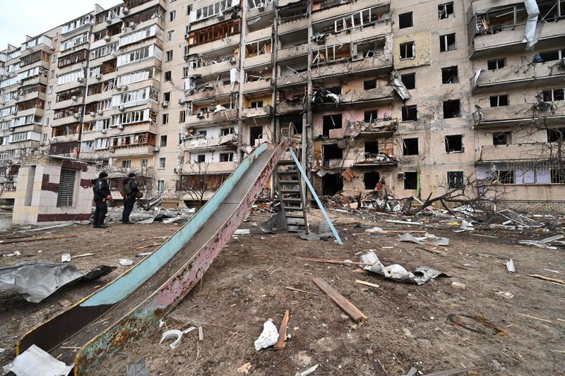Police officers stand guard at a damaged residential building at Koshytsa Street, a suburb of the Ukrainian capital Kyiv, where a military shell allegedly hit. 