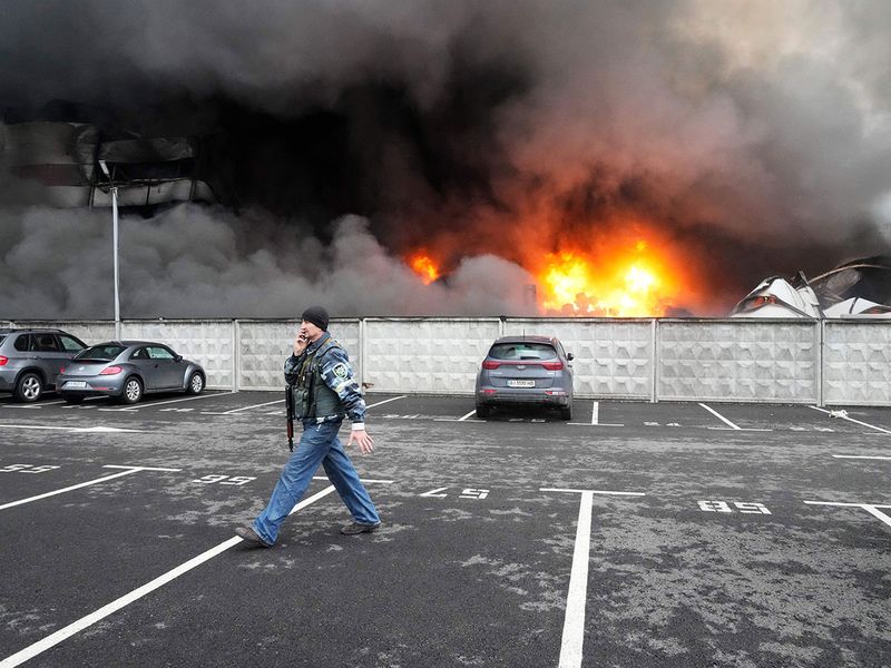 A Ukrainian serviceman walks past as fire and smoke rises over a damaged logistic center after shelling in Kyiv, Ukraine.  