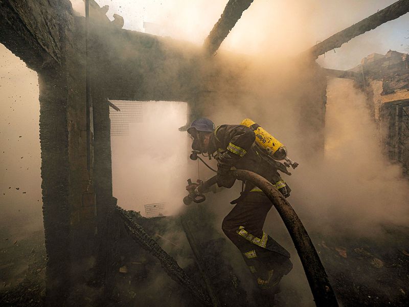 A Ukrainian firefighter sprays water inside a house destroyed by shelling in Kyiv, Ukraine. 