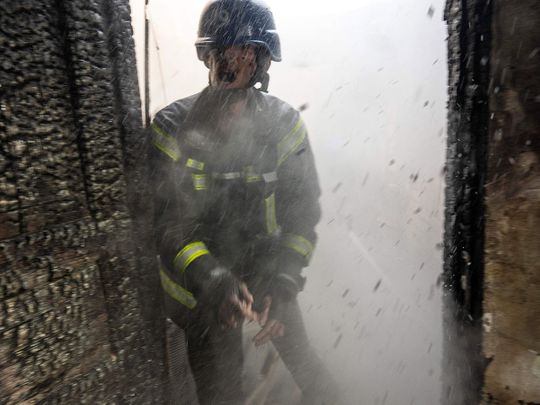 A Ukrainian firefighter shouts to a colleague while trying to extinguish a fire inside a house destroyed by shelling in Kyiv. 