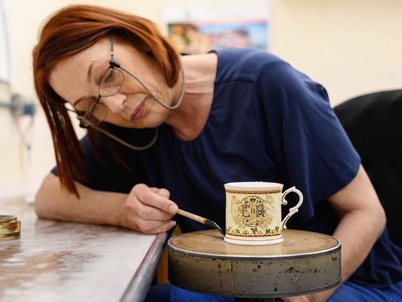Gilder Claire Wright applies gold paint by hand as she works to produce a platinum jubilee commemorative beaker for Goviers, as part of their Royal Commemoratives collection, Stoke-on-Trent. 