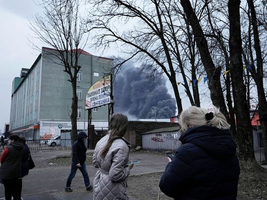 People watch smoke rising behind buildings following explosions in Lviv, western Ukraine, on Saturday, March 26, 2022. 