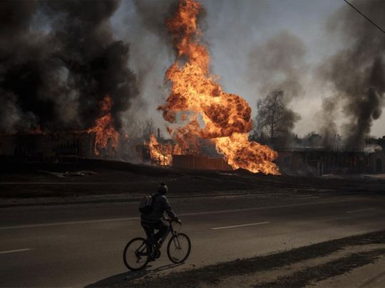 A man rides his bike past flames and smoke rising from a fire following a Russian attack in Kharkiv, Ukraine. 