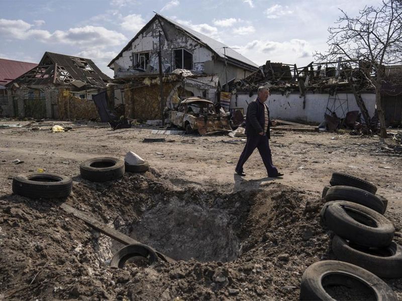 A man walks behind a crater created by a bomb and in front of damaged houses following a Russian bombing earlier this week, outskirts Mykolaiv, Ukraine.