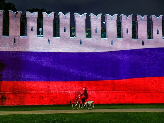 A woman rides a bicycle past a part of the Kremlin wall 