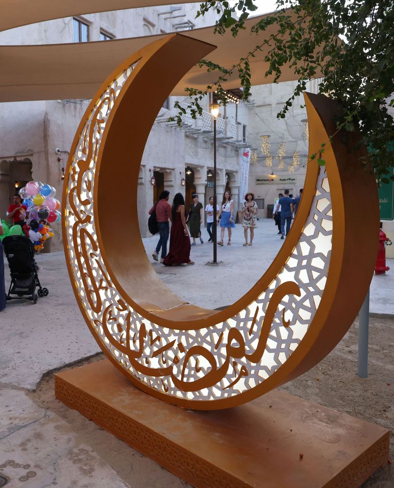 People walk past a decorative light representing the first crescent of the moon marking the start of the Muslim holy month of Ramadan, in the Seef district in the Gulf emirate of Dubai, on April 1, 2022. 