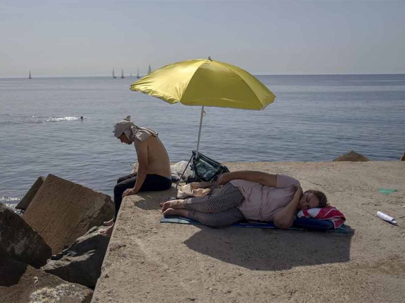 woman sleeps under an umbrella on a breakwater in front of the Mediterranean Sea in Barcelona, Spain