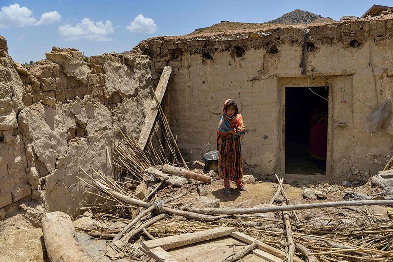 A child stands besides a house damaged by an earthquake in Bernal district, Paktika province, on June 23, 2022. - Desperate rescuers battled against the clock and heavy rain on June 23 to reach cut-off areas in eastern Afghanistan after a powerful earthquake killed at least 1,000 people and left thousands more homeless.