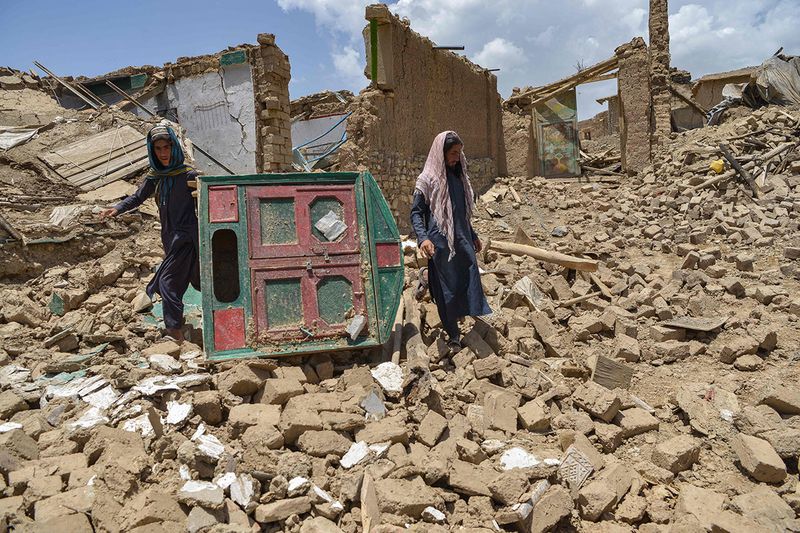 Afghan men look for their belongings amid the ruins of a house damaged by an earthquake in Bernal district, Paktika province, on June 23, 2022. - Desperate rescuers battled against the clock and heavy rain on June 23 to reach cut-off areas in eastern Afghanistan after a powerful earthquake killed at least 1,000 people and left thousands more homeless. 