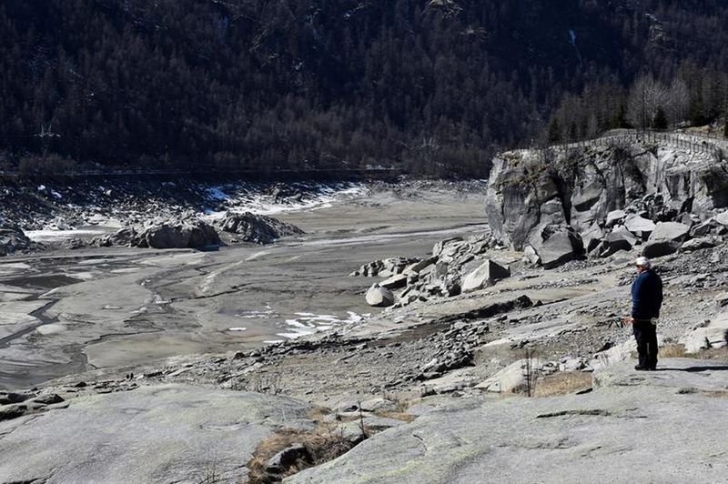 A man stands near the Ceresole Reale Lake, which provides water to the Piedmont region through a dam, dried following weeks of drought at the Gran Paradiso National Park, in Ceresole Reale, Italy, .March 24, 2022. 