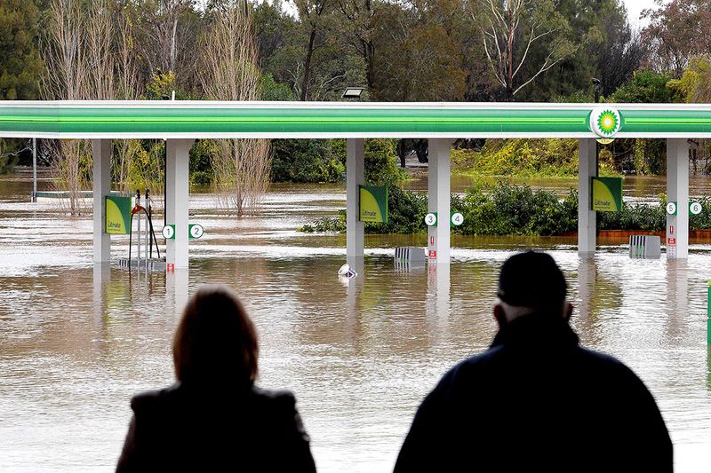 People stand next to a flooded petrol station due to torrential rain in the Camden suburb of Sydney .