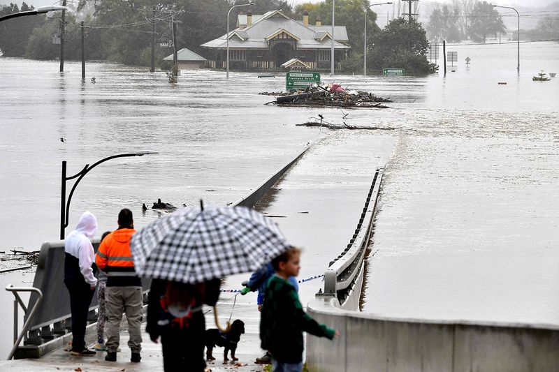 Residents look out toward flooded buildings next to the old Windsor Bridge along the overflowing Hawkesbury River in the northwestern Sydney suburb of Windsor on July 4, 2022. - Rapidly rising rivers swamped swathes of rain-lashed Sydney on July 4, forcing thousands to flee 