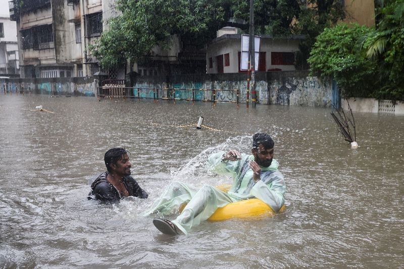 A man splashes water on another amidst heavy rainfall on a flooded street in Mumbai.