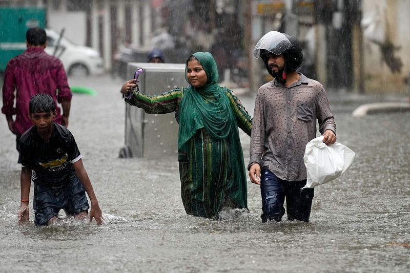 A woman takes a selfie as she walks past a water logged street during heavy rainfall in Mumbai, India, Tuesday, July 5, 2022. 