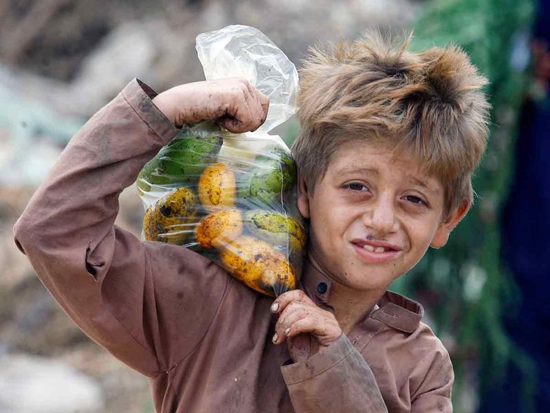 An Afghan refugee boy carries a bag of mangoes on his shoulder in Karachi, Pakistan. 