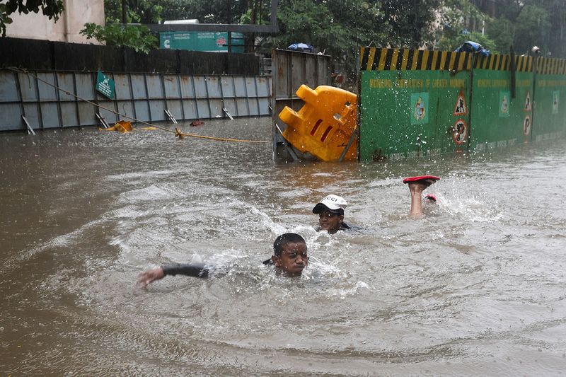 Boys swim on a flooded street amidst heavy rainfall.