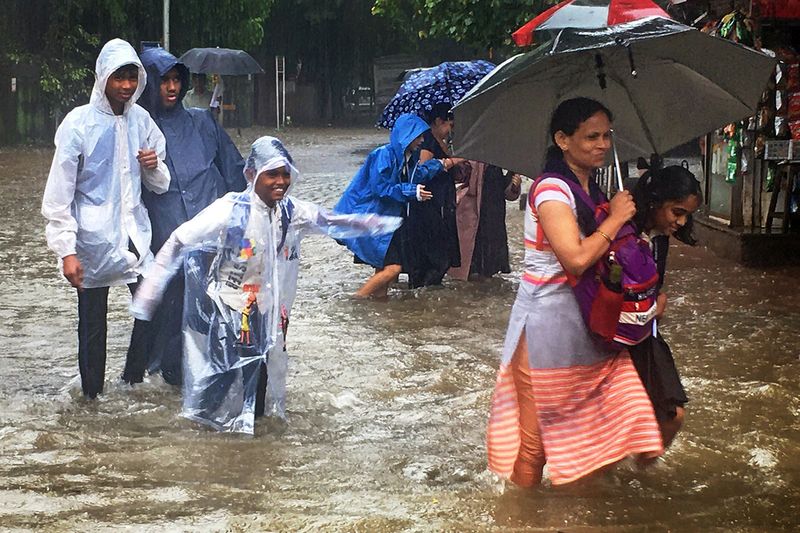 Students wearing raincoats cross a heavily waterlogged road during rainfall, at Matunga, in Mumbai on Tuesday. 