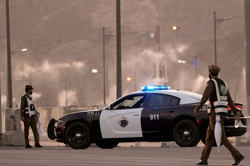 Water mist is sprayed as Saudi policemen stand alert at a check point in the Arafat tent camp, in the Saudi Arabia's holy city of Mecca, Tuesday, July 5, 2022. Saudi Arabia is expected to receive one million Muslims to attend Hajj pilgrimage, which will begin on July 7, after two years of limiting the numbers because coronavirus pandemic.