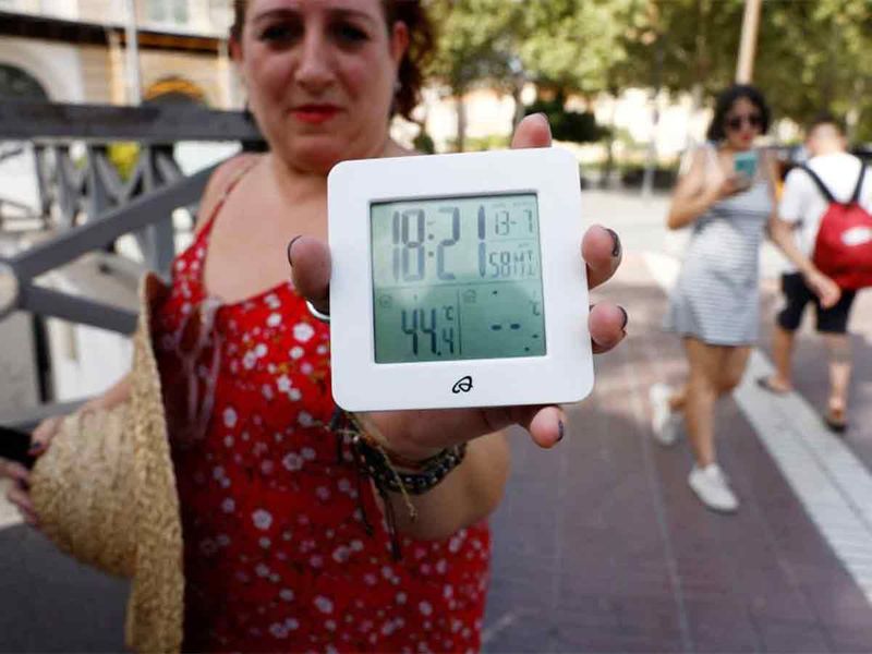 A woman shows a thermometer displaying 44 degree Celsius (111.2 degree Fahrenheit) in a street during the second heatwave of the year, in Seville, southern Spain, July 13, 2022. 