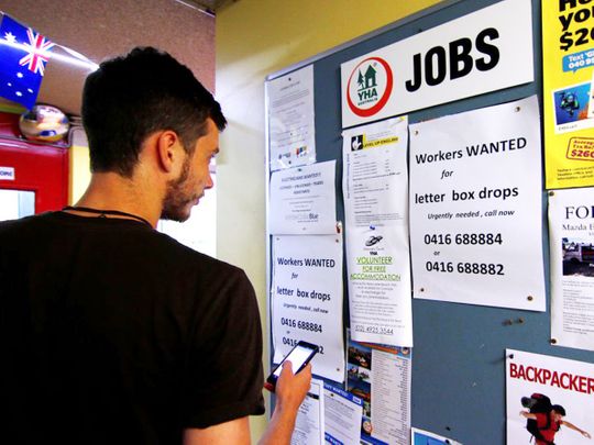A man uses his phone to record a job add posted on a notice board at a backpacker hostel in Sydney. 